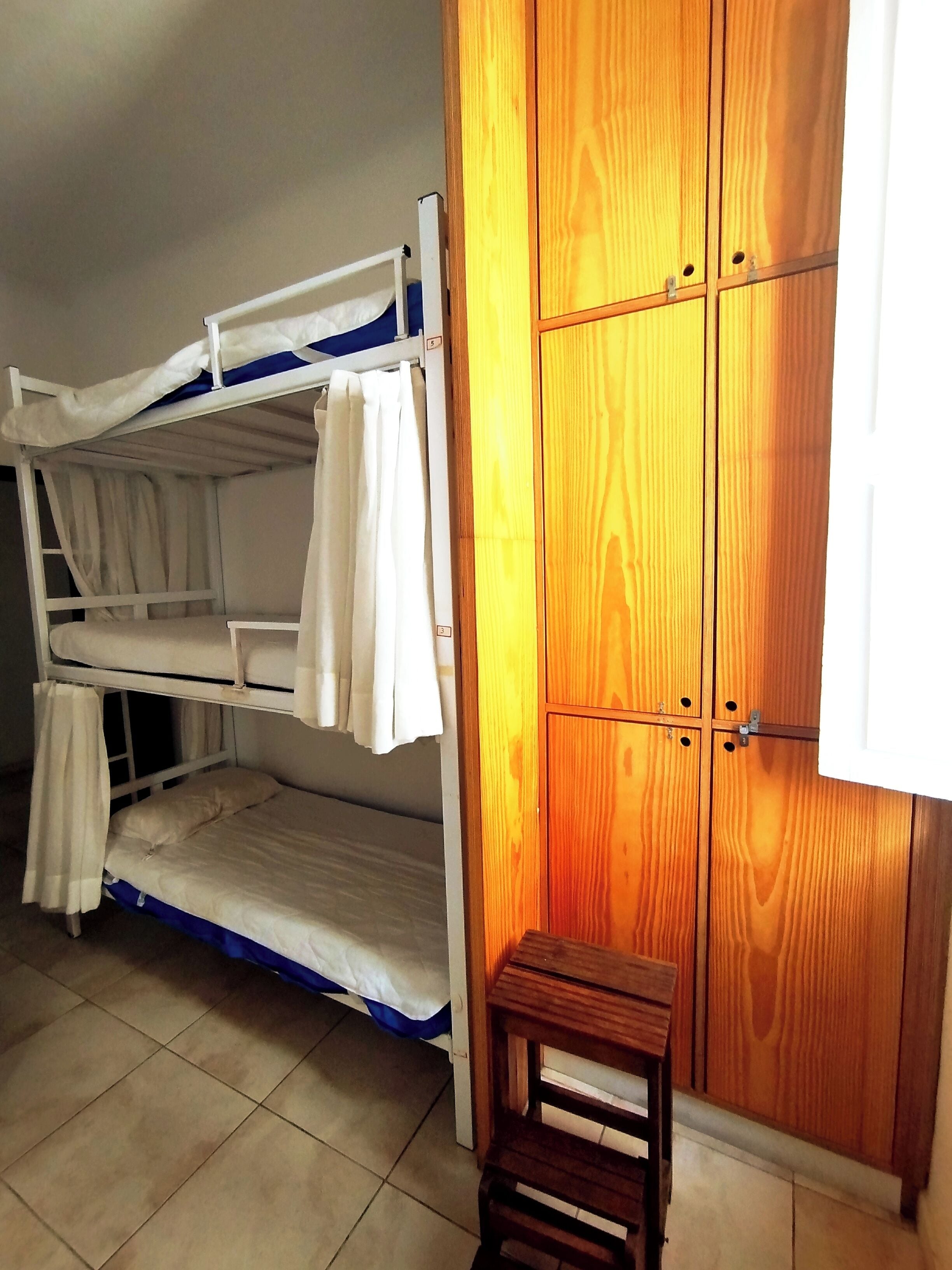 A bunk bed with white bedding, a wooden wardrobe, and a small wooden stool.