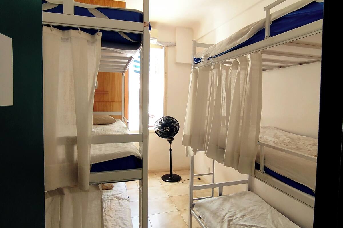 A dormitory room with bunk beds, a standing fan, and a door with a lock.