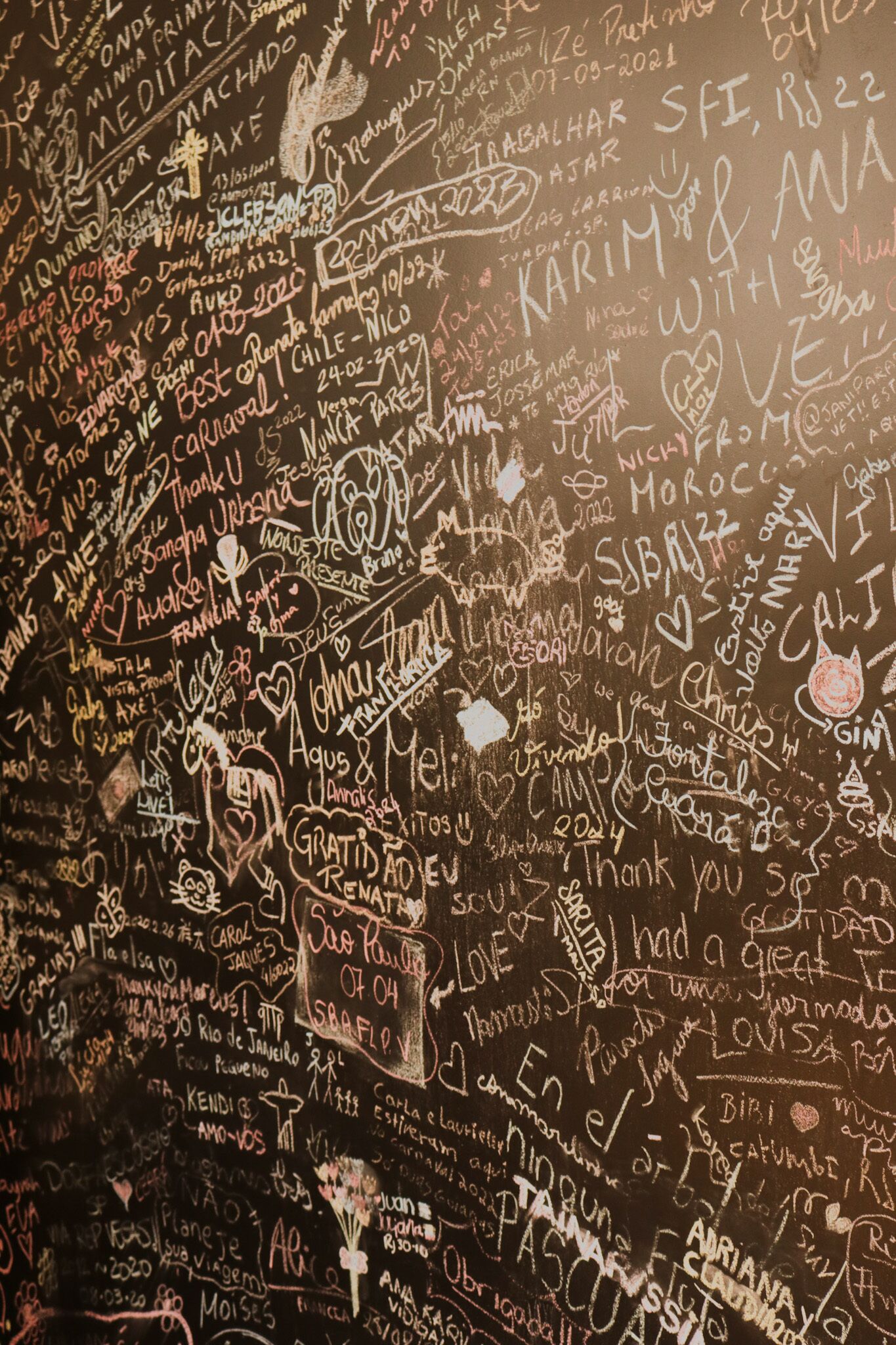 A wall covered with various handwritten messages and drawings, including names, dates, and doodles.