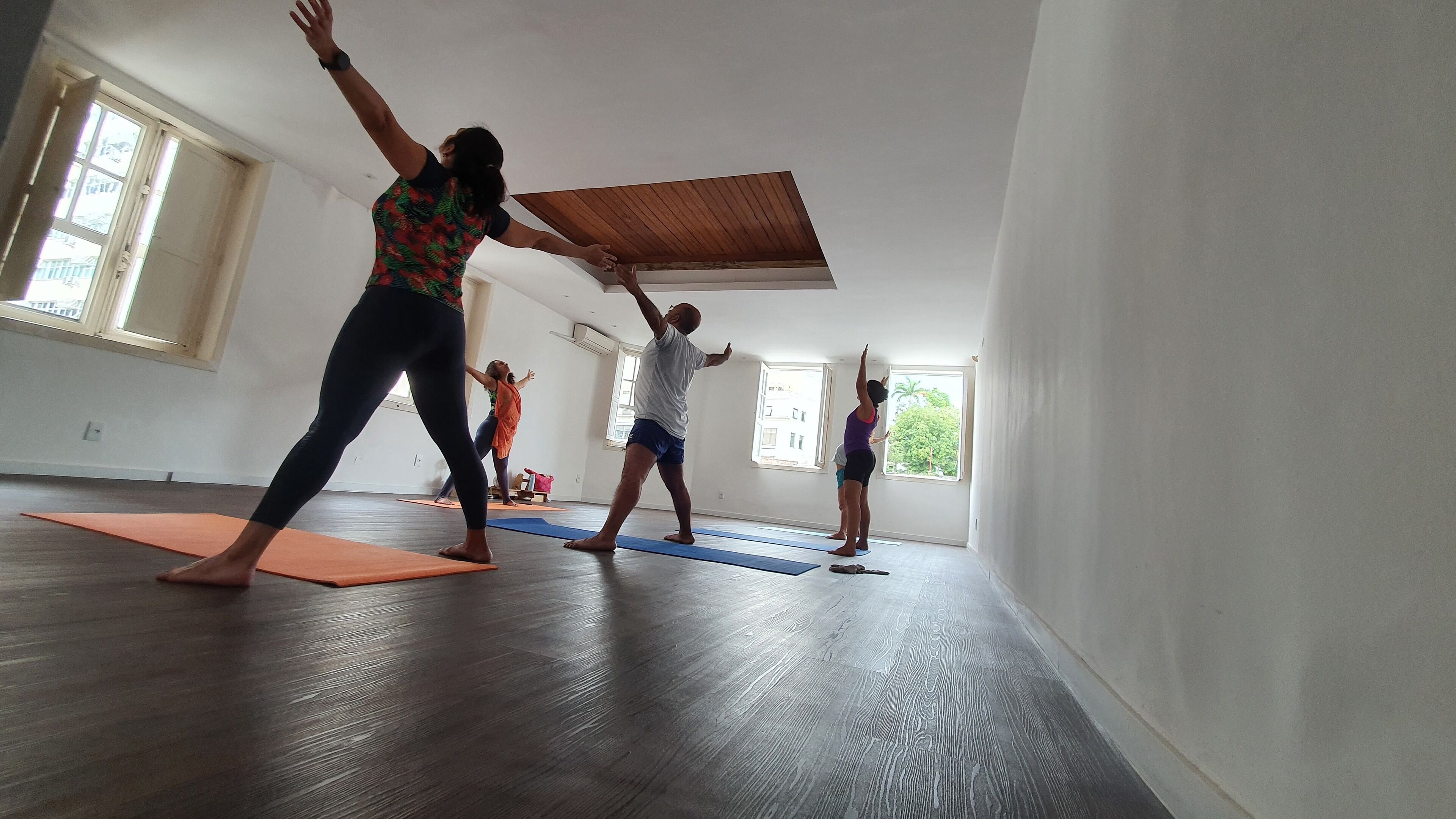 A spacious room with large windows, wooden flooring, and yoga mats on the floor.