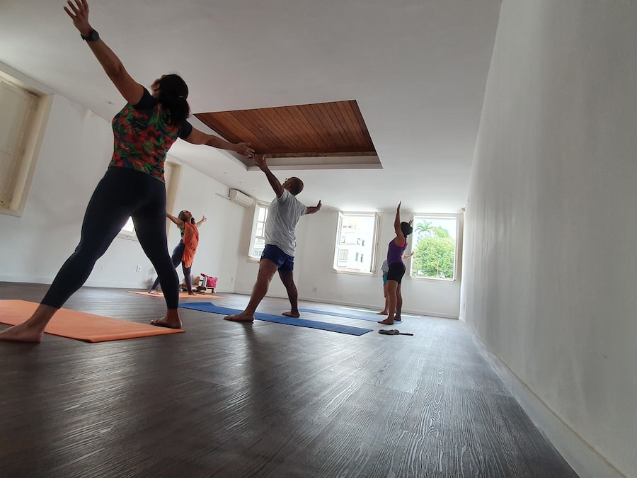 A spacious room with large windows, wooden flooring, and yoga mats on the floor.
