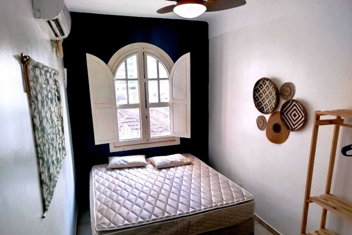 Quarto com cama, janela, ar condicionado fixado na parede e escada de madeira.