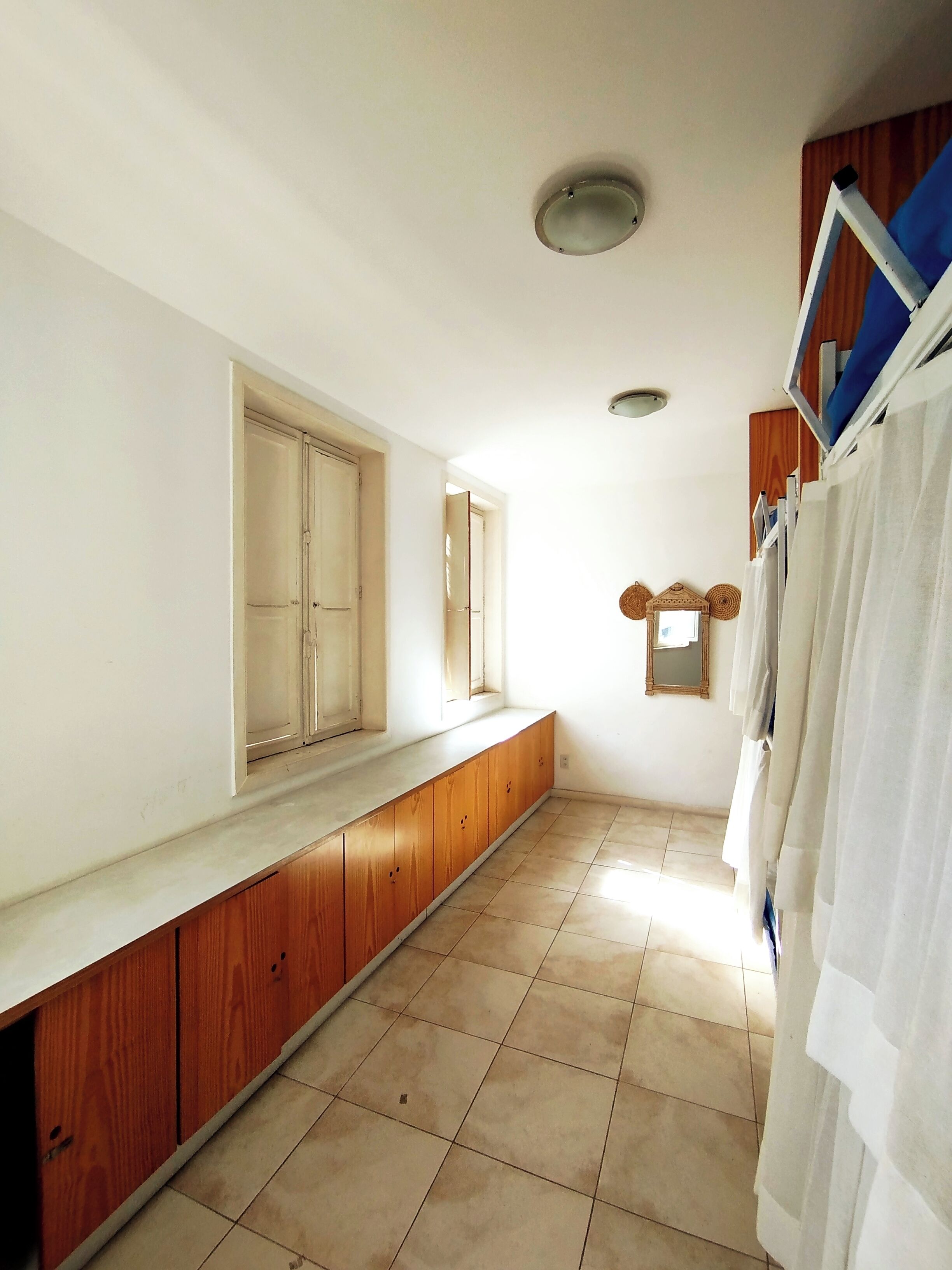 A room with a long wooden bench, a window, a mirror, and a ceiling light fixture.