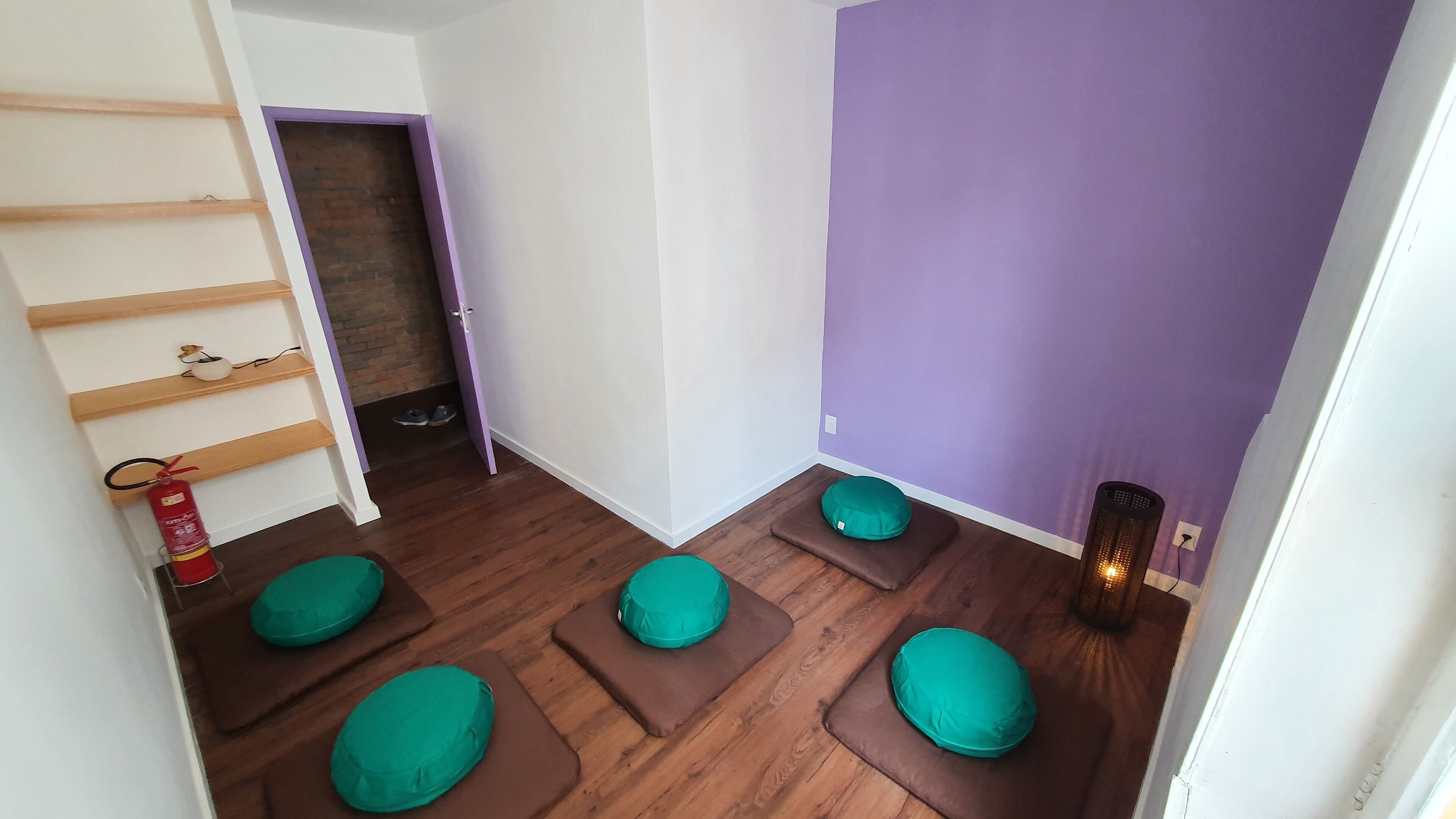 A room with a purple wall, wooden flooring, and green cushioned seating areas.