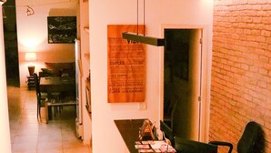 A modern living room with a wooden floor, a dining area in the background, and a brick wall. - Sangha Urbana - hostel, yoga & meditation (Rio de Janeiro)