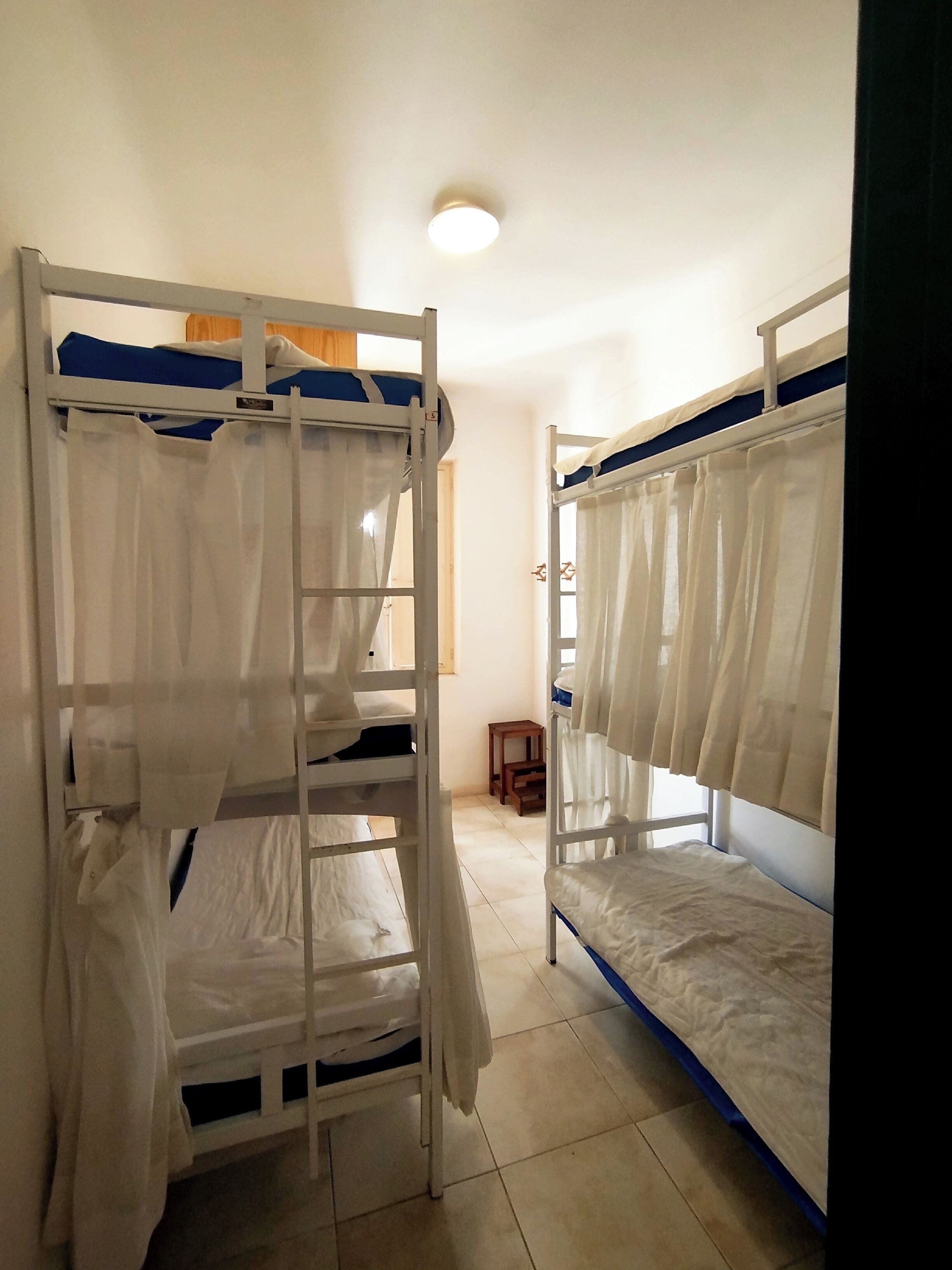 A dormitory room with bunk beds, a small table, and a window with curtains.