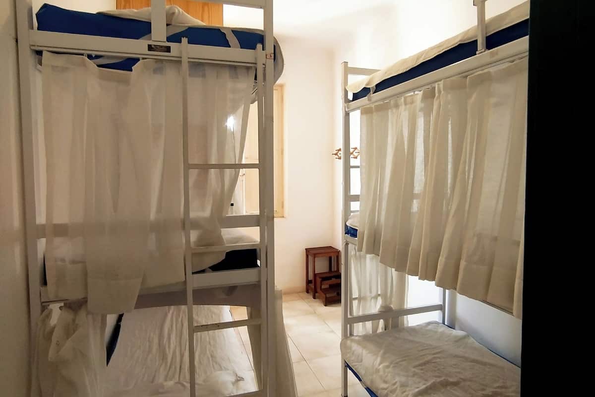A dormitory room with bunk beds, a small table, and a window with curtains.