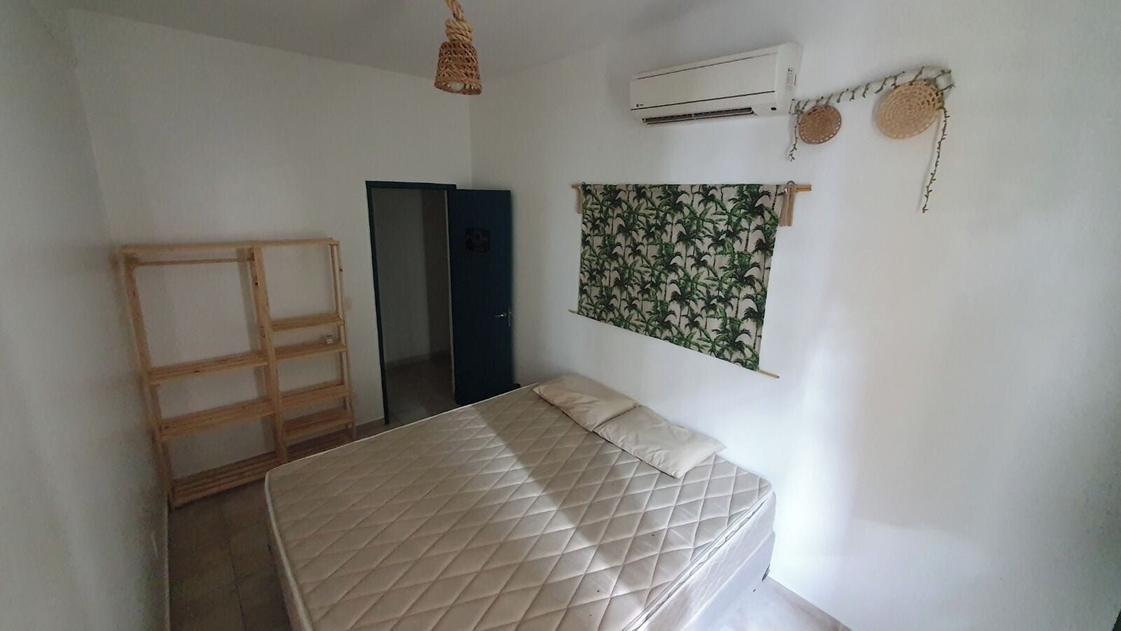 Un dormitorio con cama, aire acondicionado, armario y puerta que da a otra habitación.