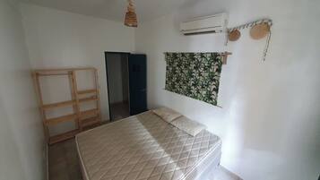 Un dormitorio con cama, aire acondicionado, armario y puerta que da a otra habitación.