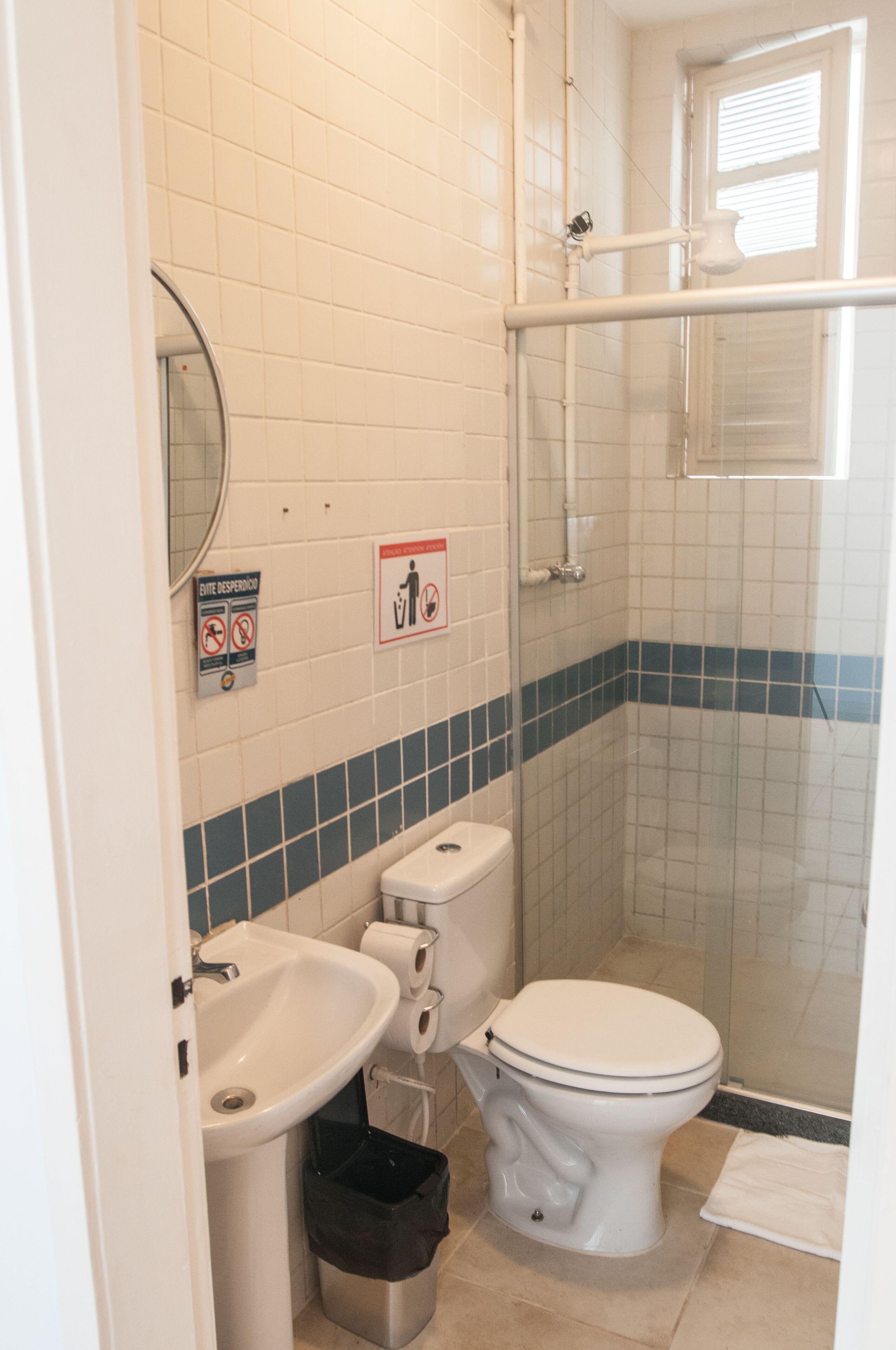 Et badeværelse med toilet, vask og brusebad. Der er skilte på væggen og en skraldespand.