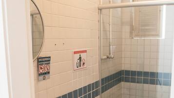 Et badeværelse med toilet, vask og brusebad. Der er skilte på væggen og en skraldespand.