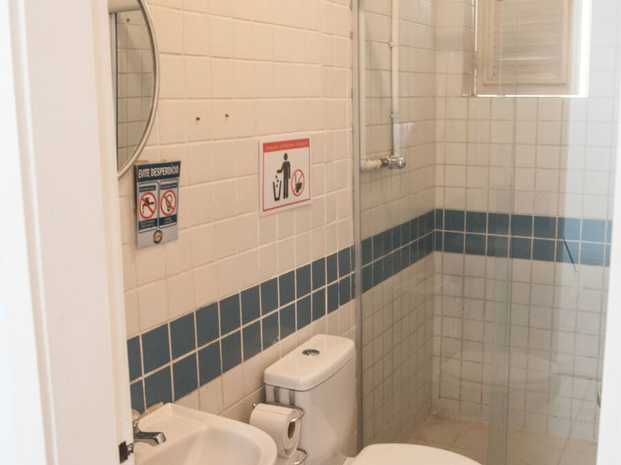 A bathroom with a toilet, sink, and shower. There are signs on the wall and a trash can.