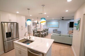 A modern kitchen with stainless steel appliances, a central island with a sink, pendant lighting, and a dining area with a table and chairs.