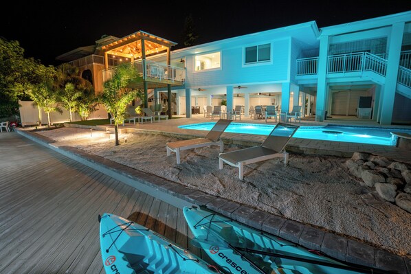 A two-story house with a swimming pool, lounge chairs, and kayaks.