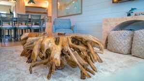 Ein Esstisch aus Naturholz mit außergewöhnlichem Design, umgeben von Stühlen und einer Couch in einem gut beleuchteten Raum mit Kamin und Wandbildern.