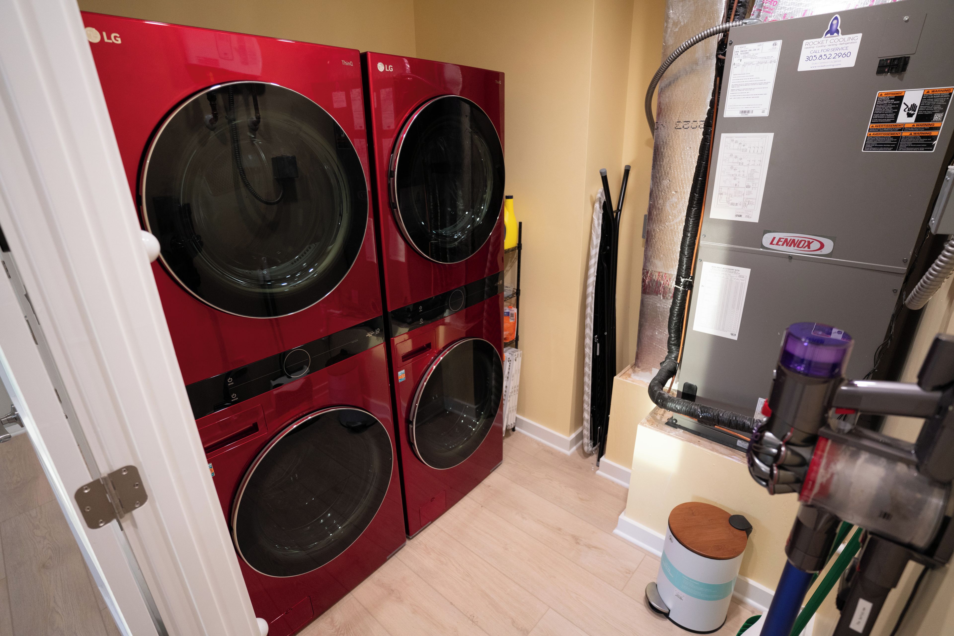 A laundry room with four red LG front-loading washing machines, a Lennox air conditioning unit, and a trash can.