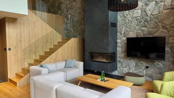 A modern living room with a stone wall, a fireplace, a flat-screen TV, and a wooden staircase.