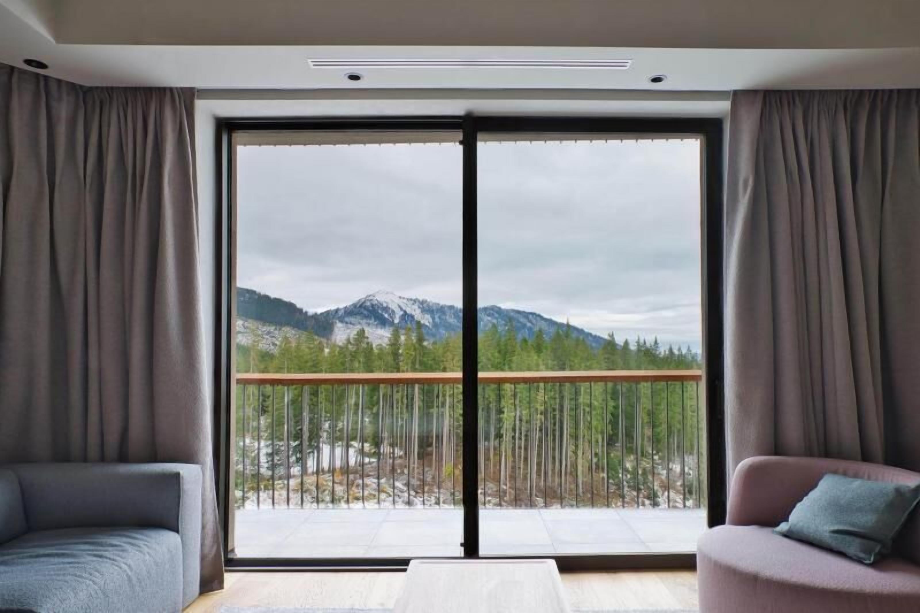 A modern room with a large sliding glass door leading to a balcony with a mountain view.