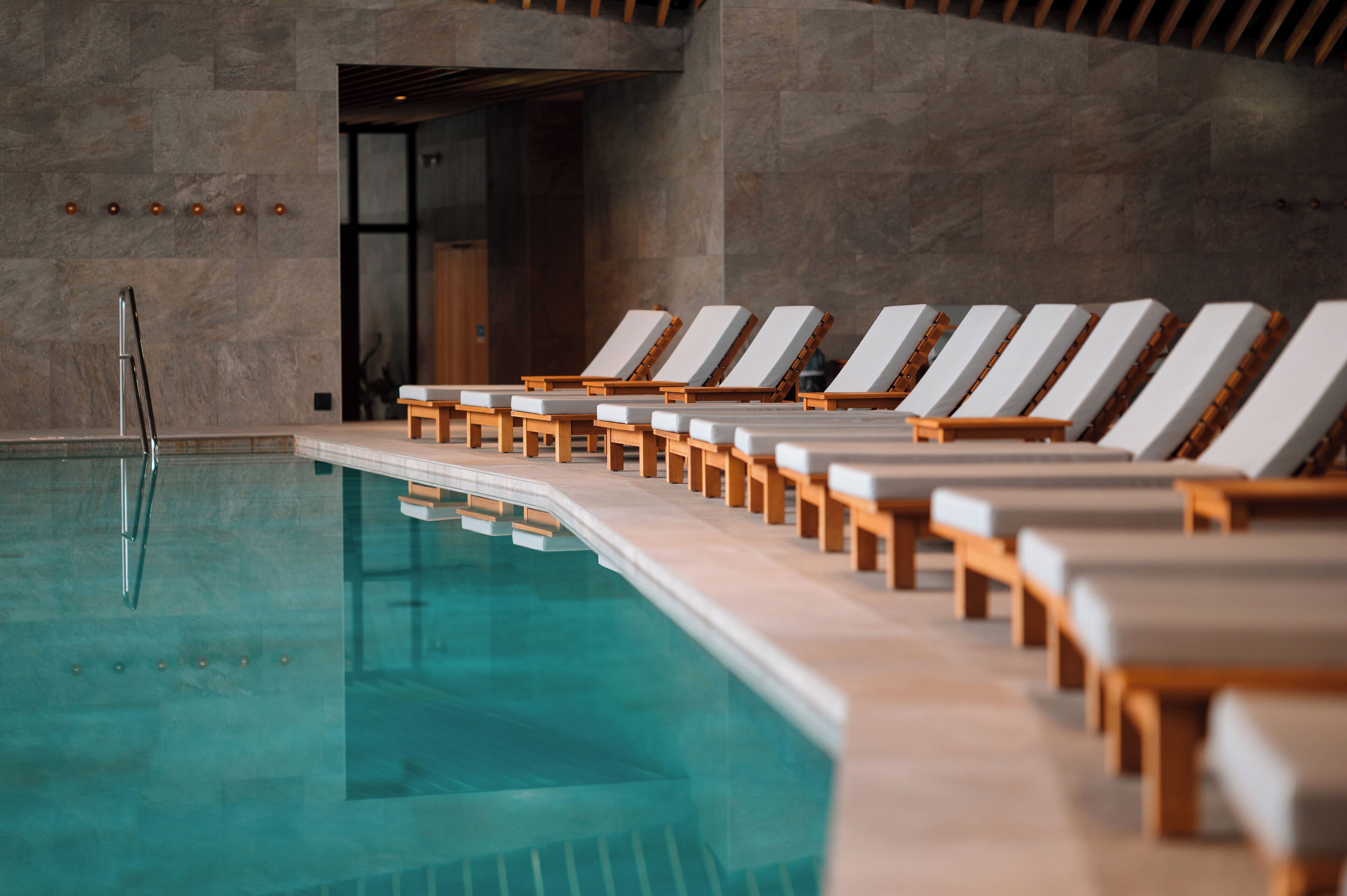 A swimming pool with wooden loungers aligned along its edge.
