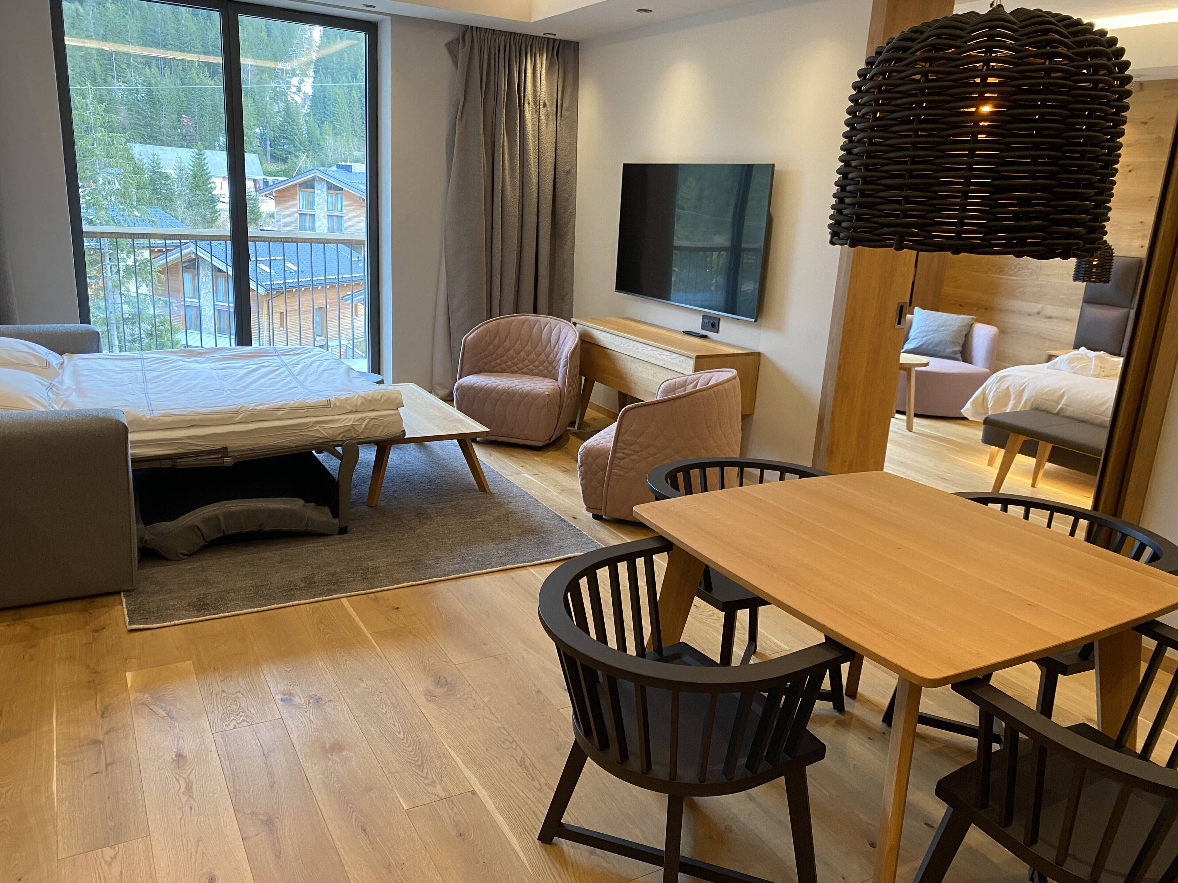 A modern hotel room with a bed, a desk, a chair, a TV, and a view of the outside.
