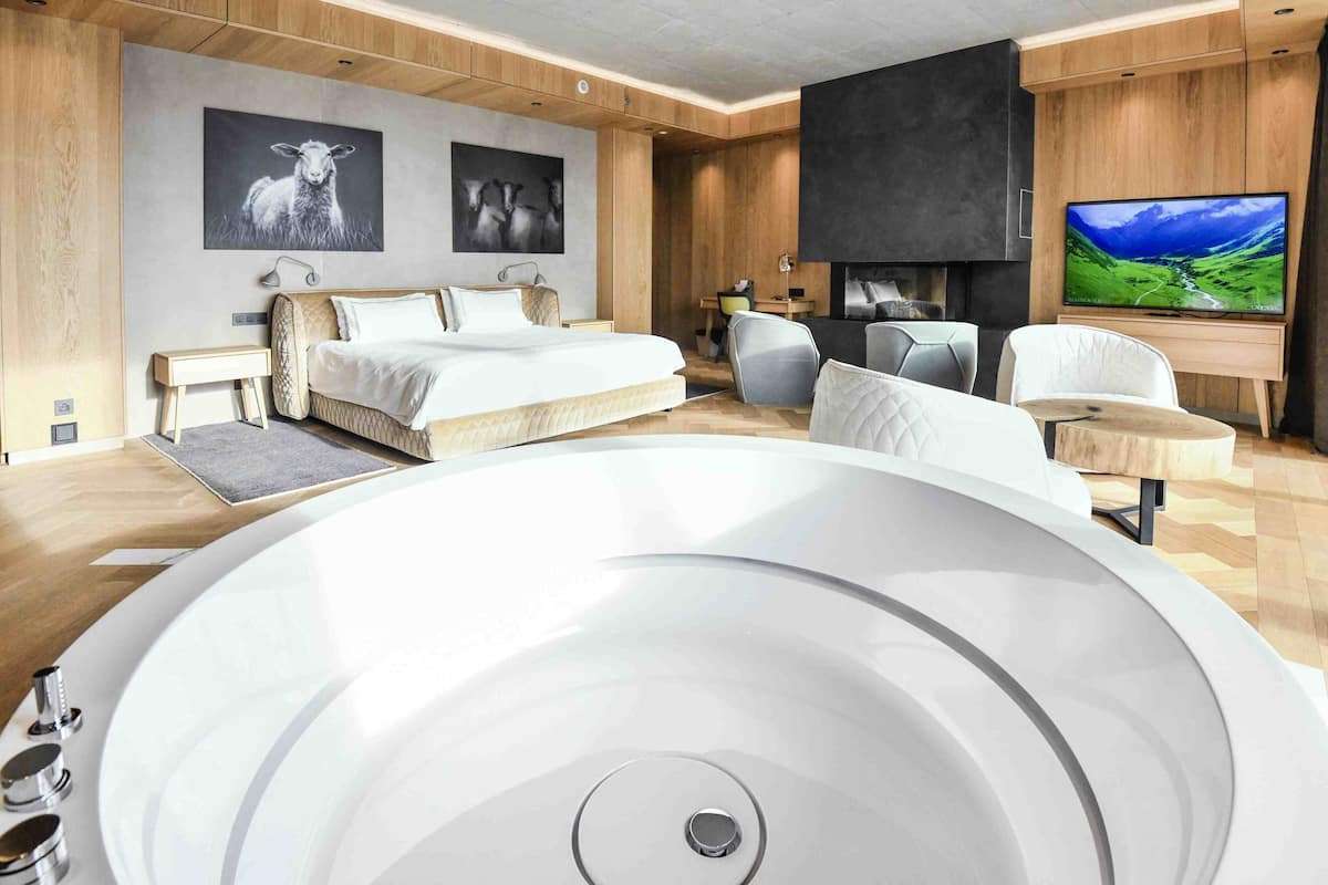 A modern bedroom with a large bed, a TV, and a fireplace.