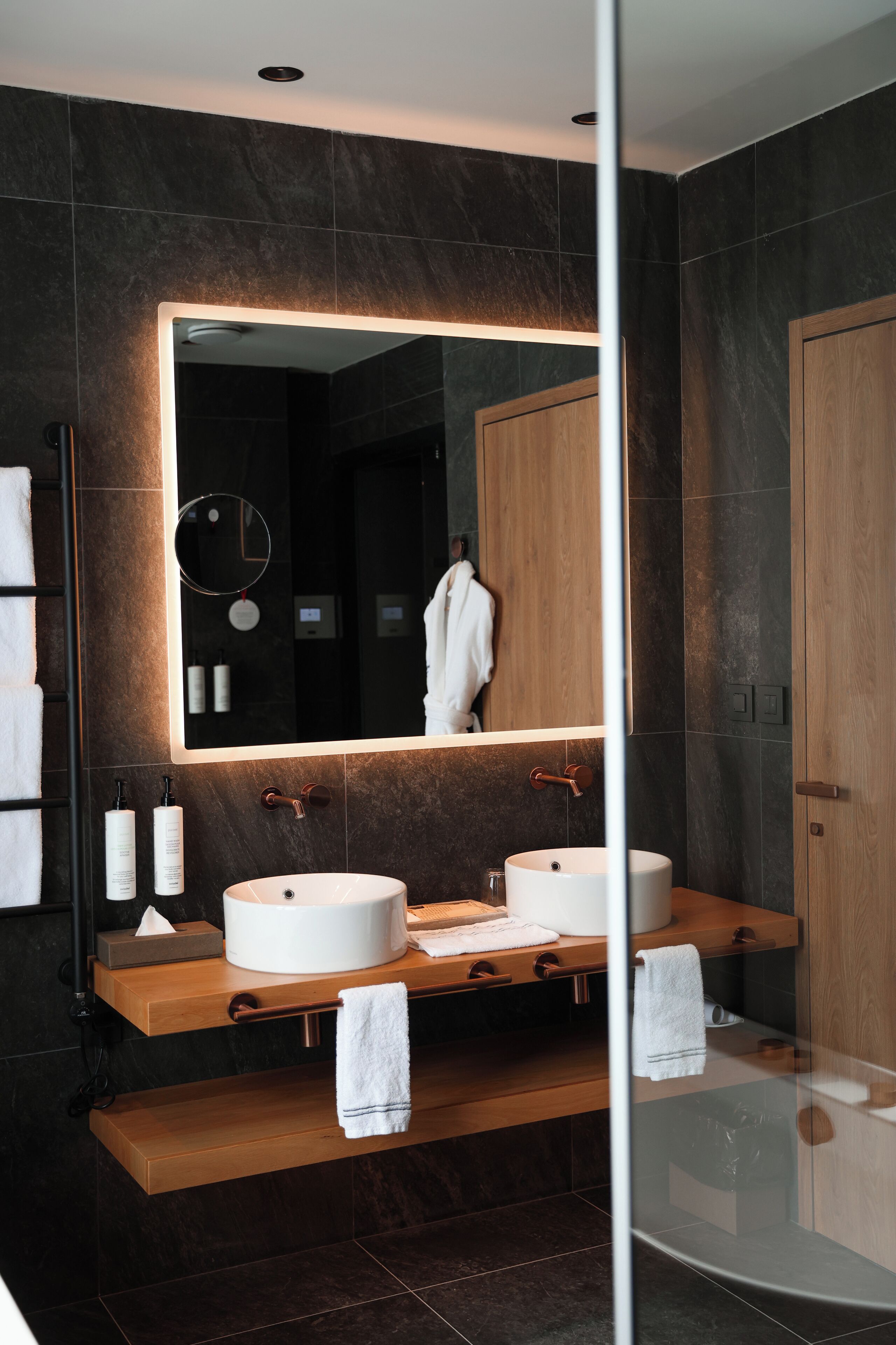 A modern bathroom with two sinks, a large mirror, and wooden vanity.