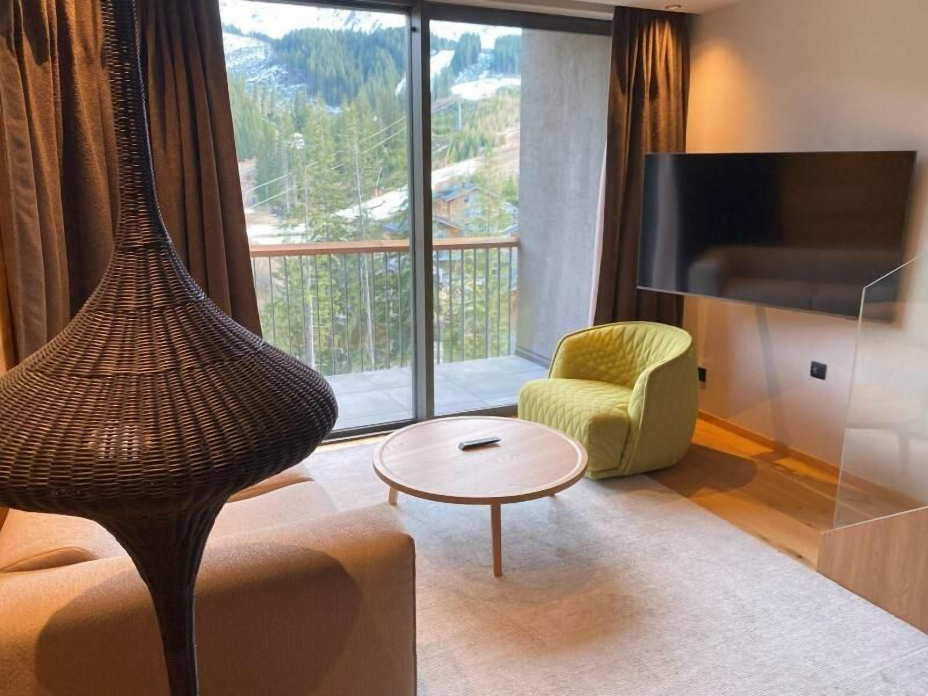 A modern hotel room with a large window offering a scenic view of trees and mountains.