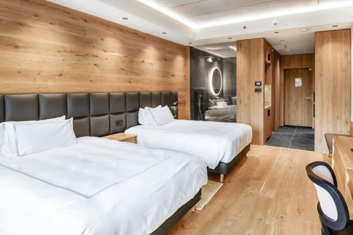 A hotel room with two beds, a wooden wall, a modern headboard, and a small desk with a chair.