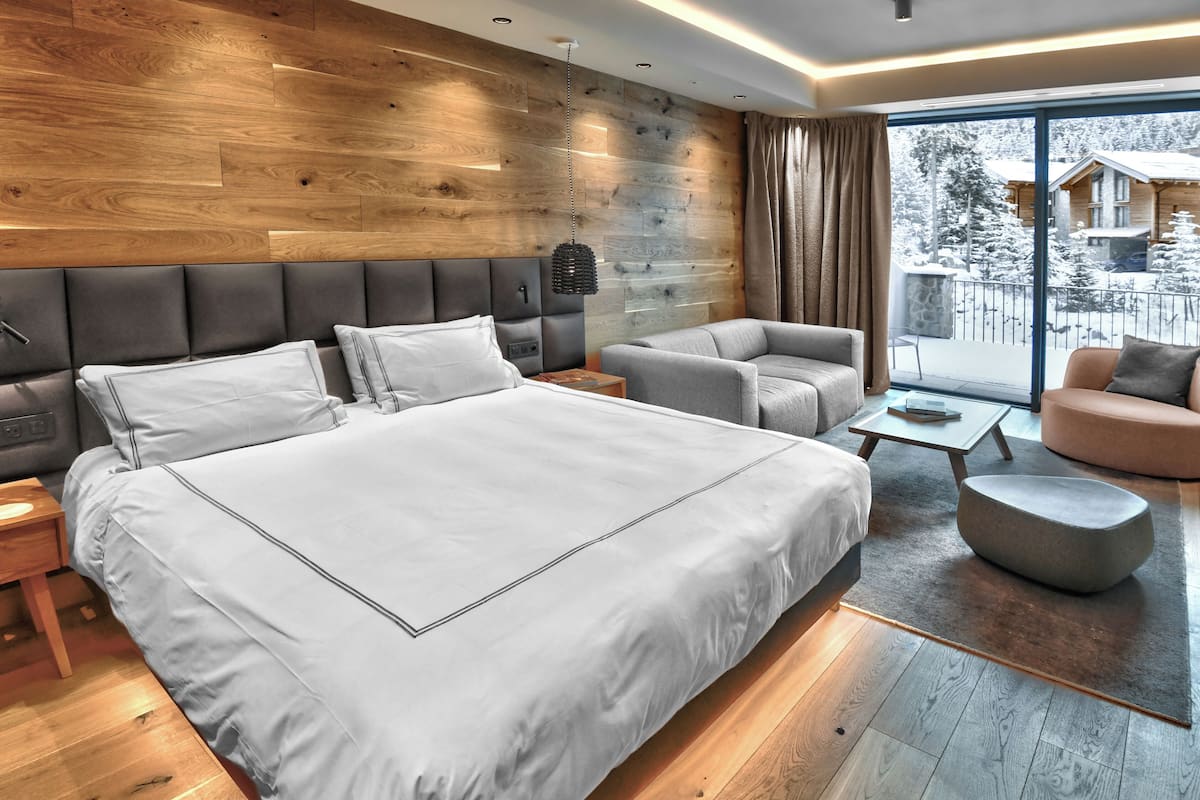A modern bedroom with a large bed, two armchairs, a sofa, and a view of a snowy landscape.
