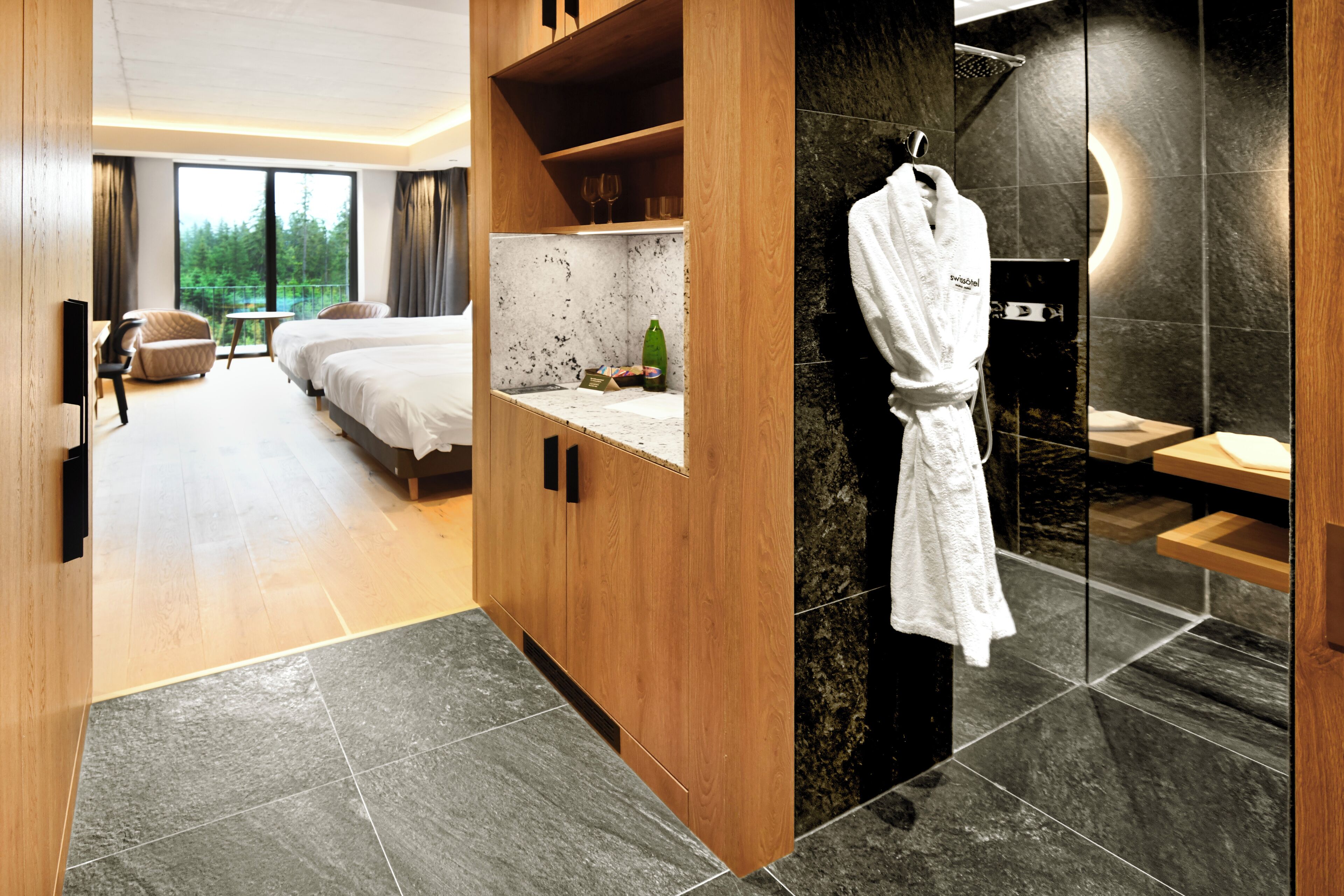Ein Hotelzimmer mit einem Holzschrank, einem Bett, einem kleinen Tisch mit einer Flasche und einem auf einem Haken hängenden Bademantel.