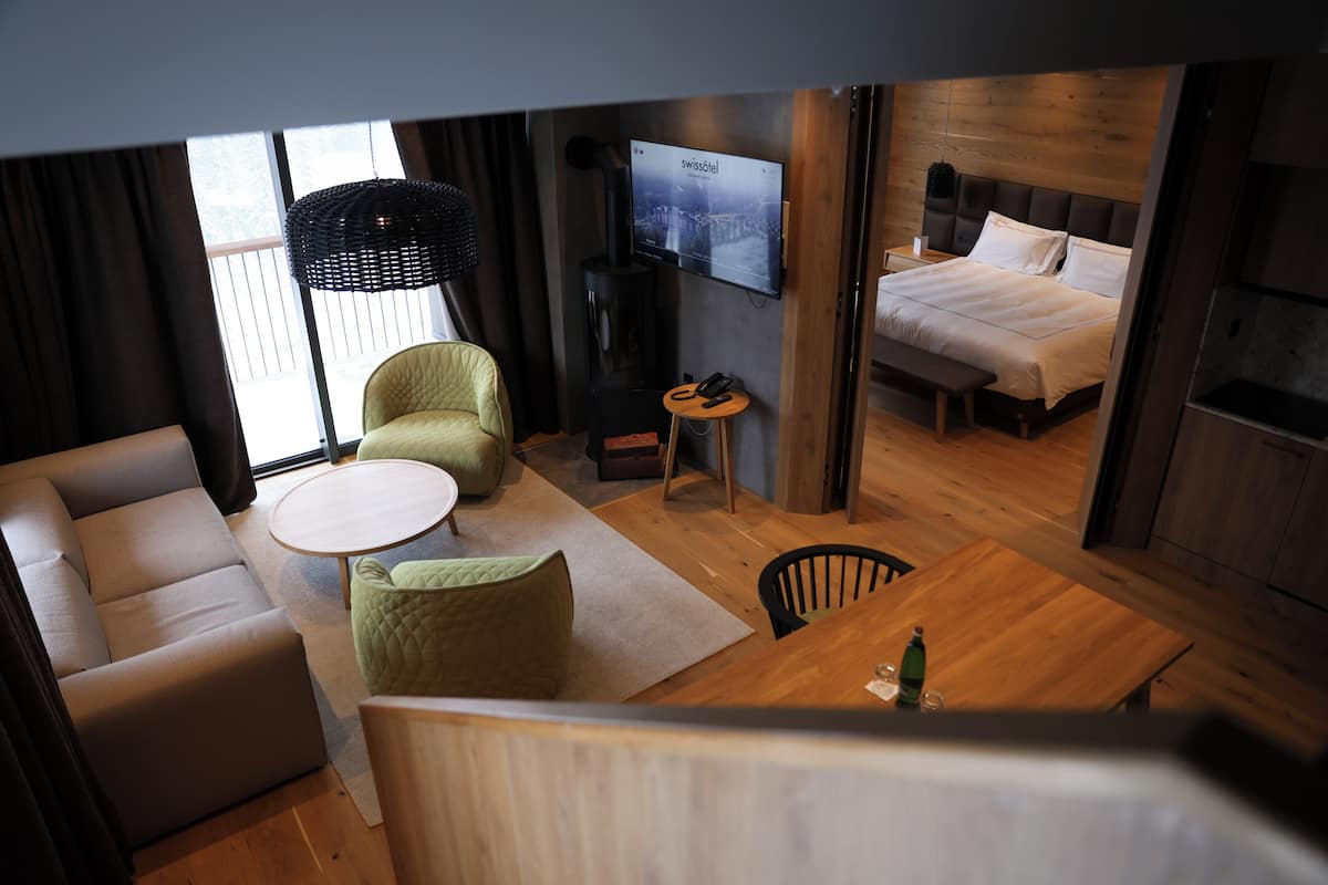 A modern hotel room with a sofa, a dining table, a TV, and a bed.