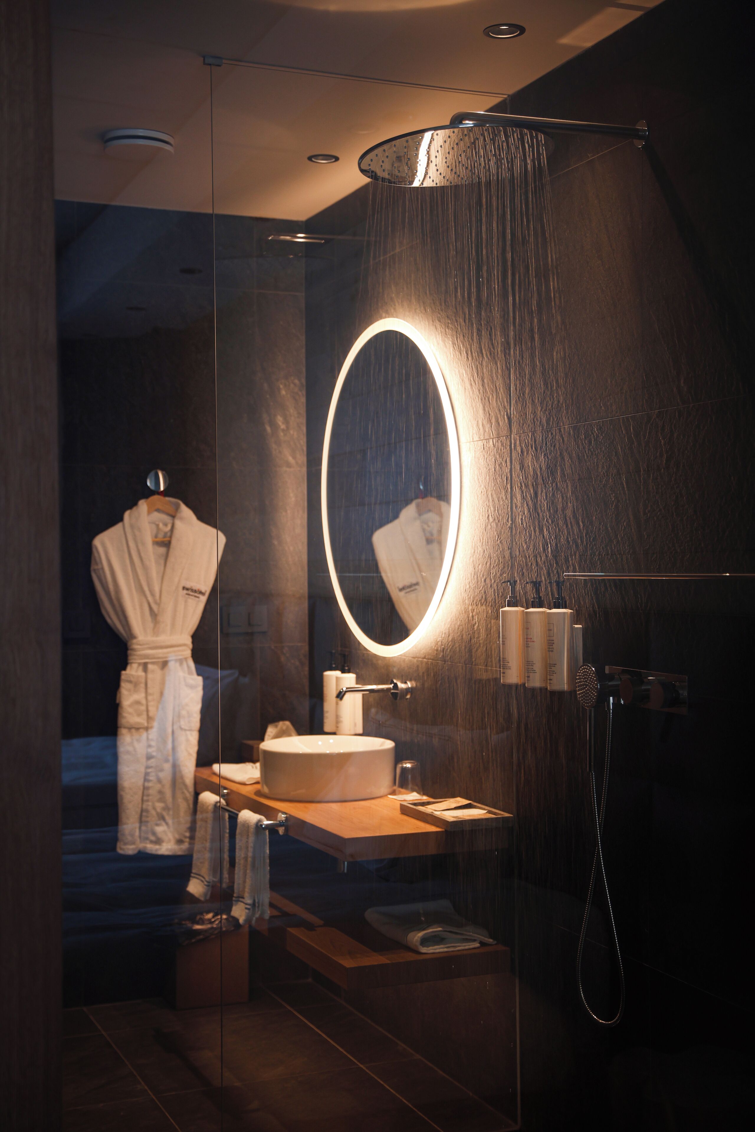 Une salle de bain moderne avec une douche à parois de verre, un miroir rond et un meuble-lavabo en bois.