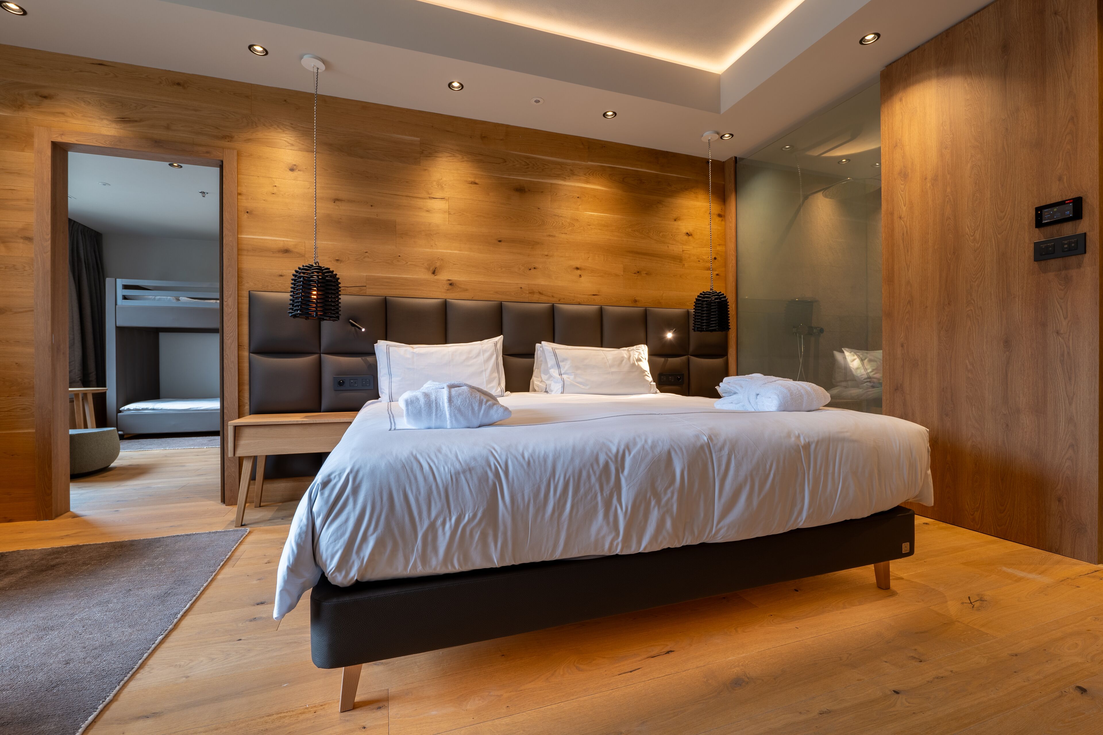 A modern bedroom with a large bed, wooden panel walls, and a built-in bench.