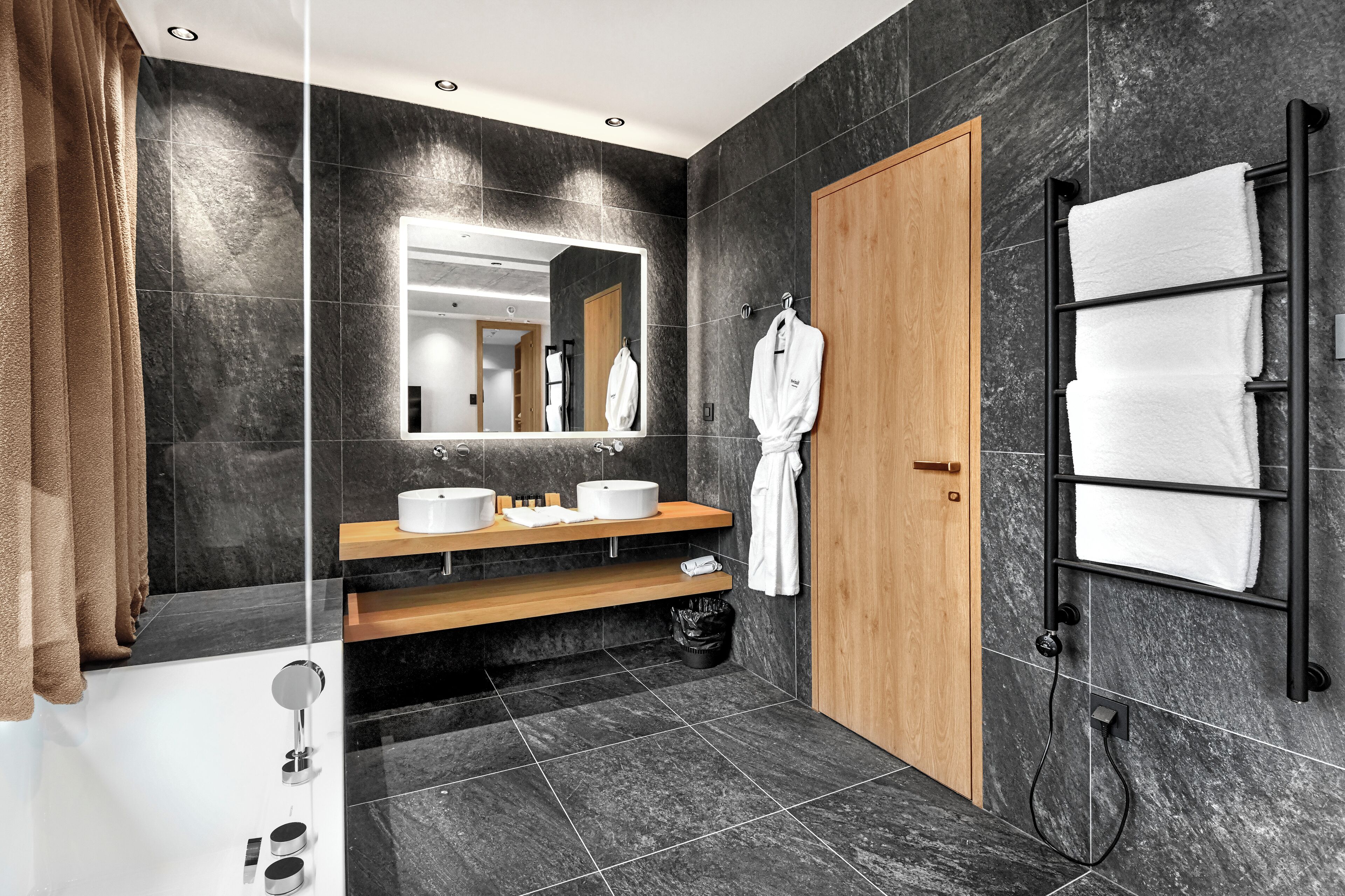 Une salle de bain moderne avec un meuble-lavabo en bois, un grand miroir, un porte-serviettes et une baignoire.