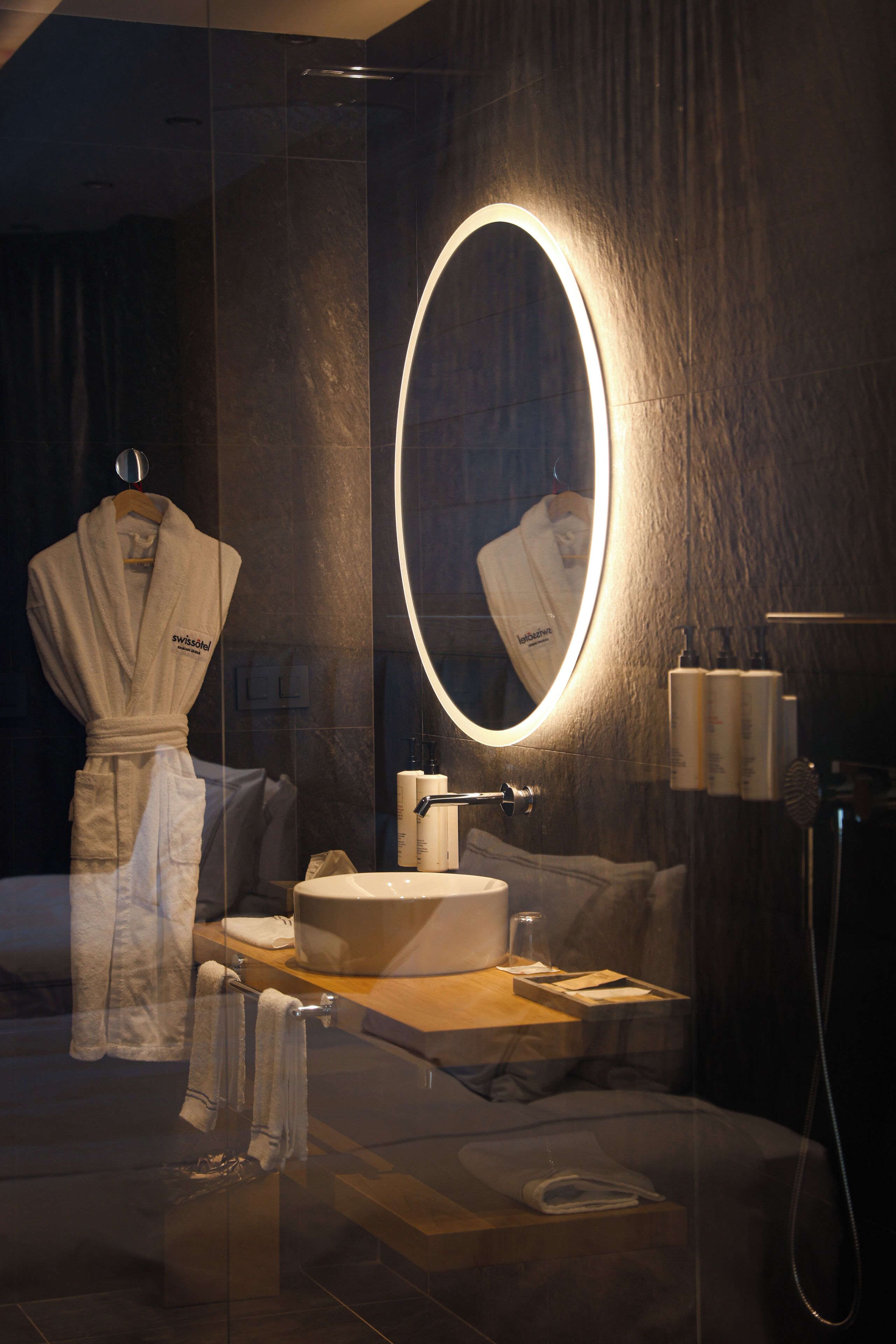 Un bagno moderno con uno specchio rotondo, un accappatoio, un lavandino e articoli da toilette.