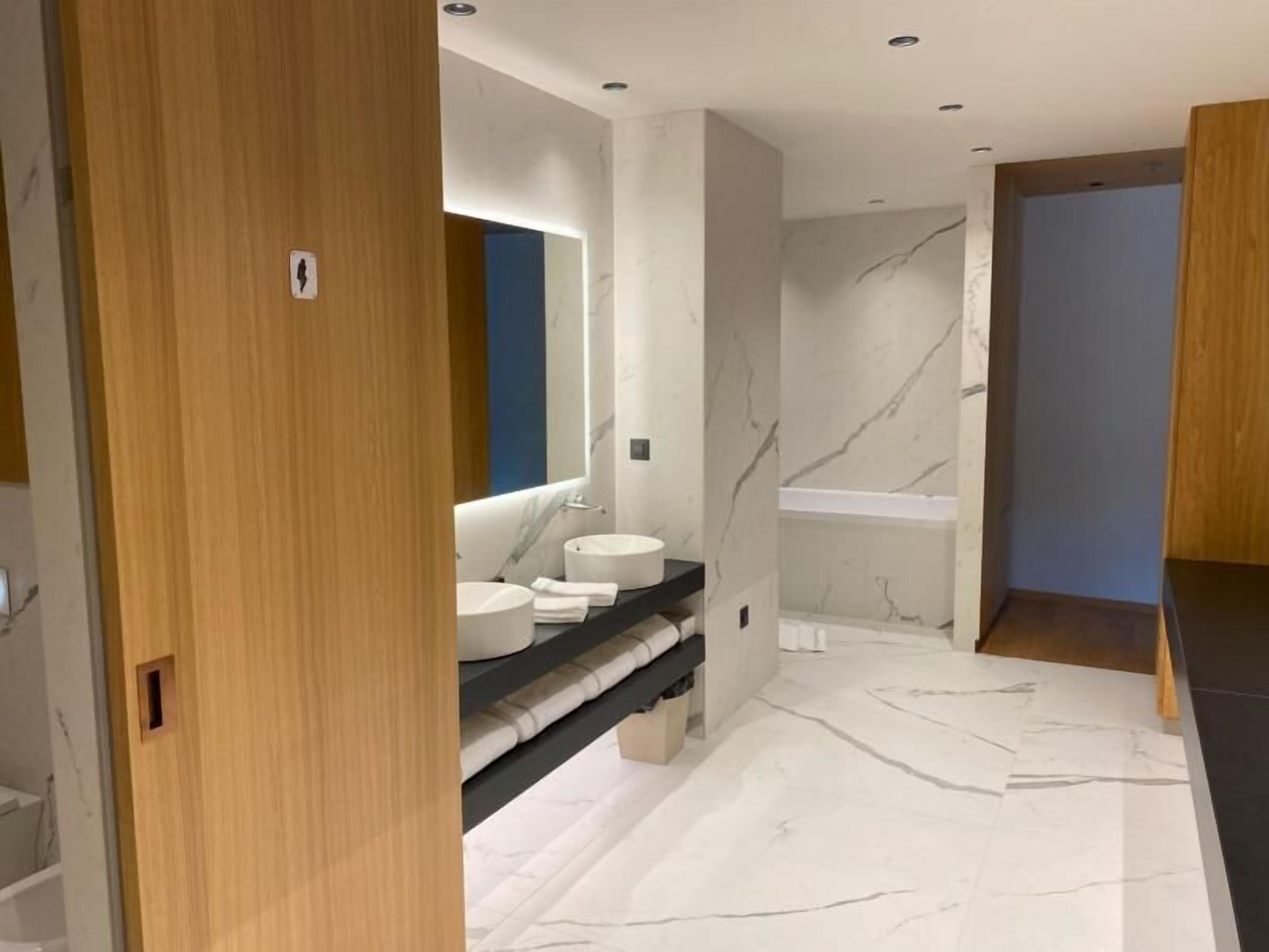 A modern bathroom with a marble floor, a large mirror, and a black countertop with two sinks.