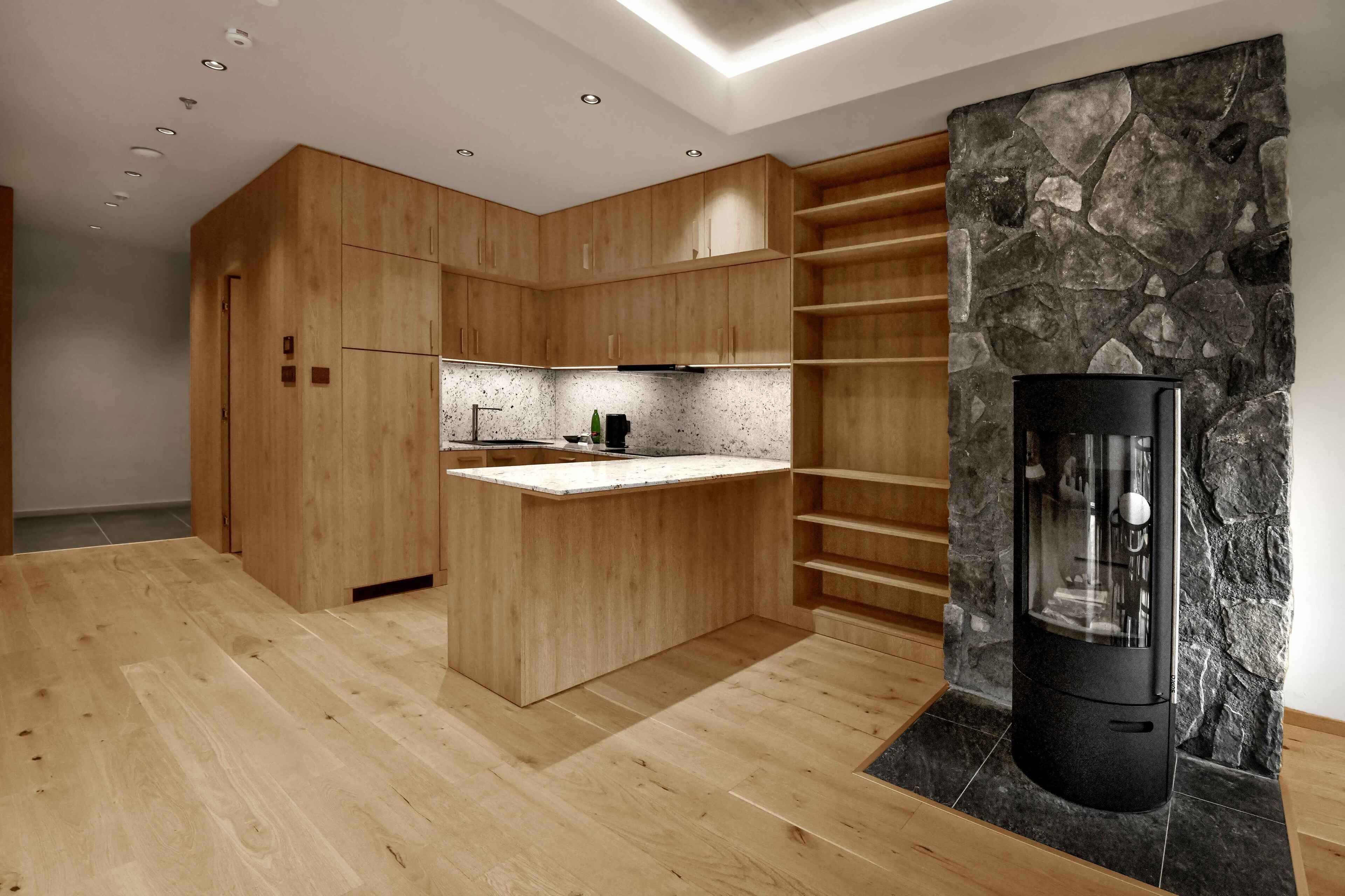 A modern kitchen with wooden cabinetry, a marble countertop, and a built-in stone wall.