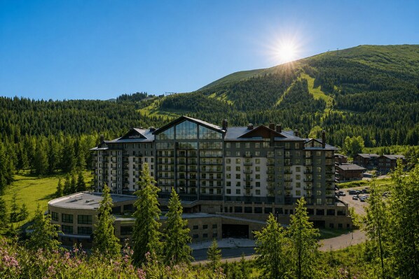 Un gran hotel con varios pisos, rodeado de un área boscosa y una montaña al fondo.