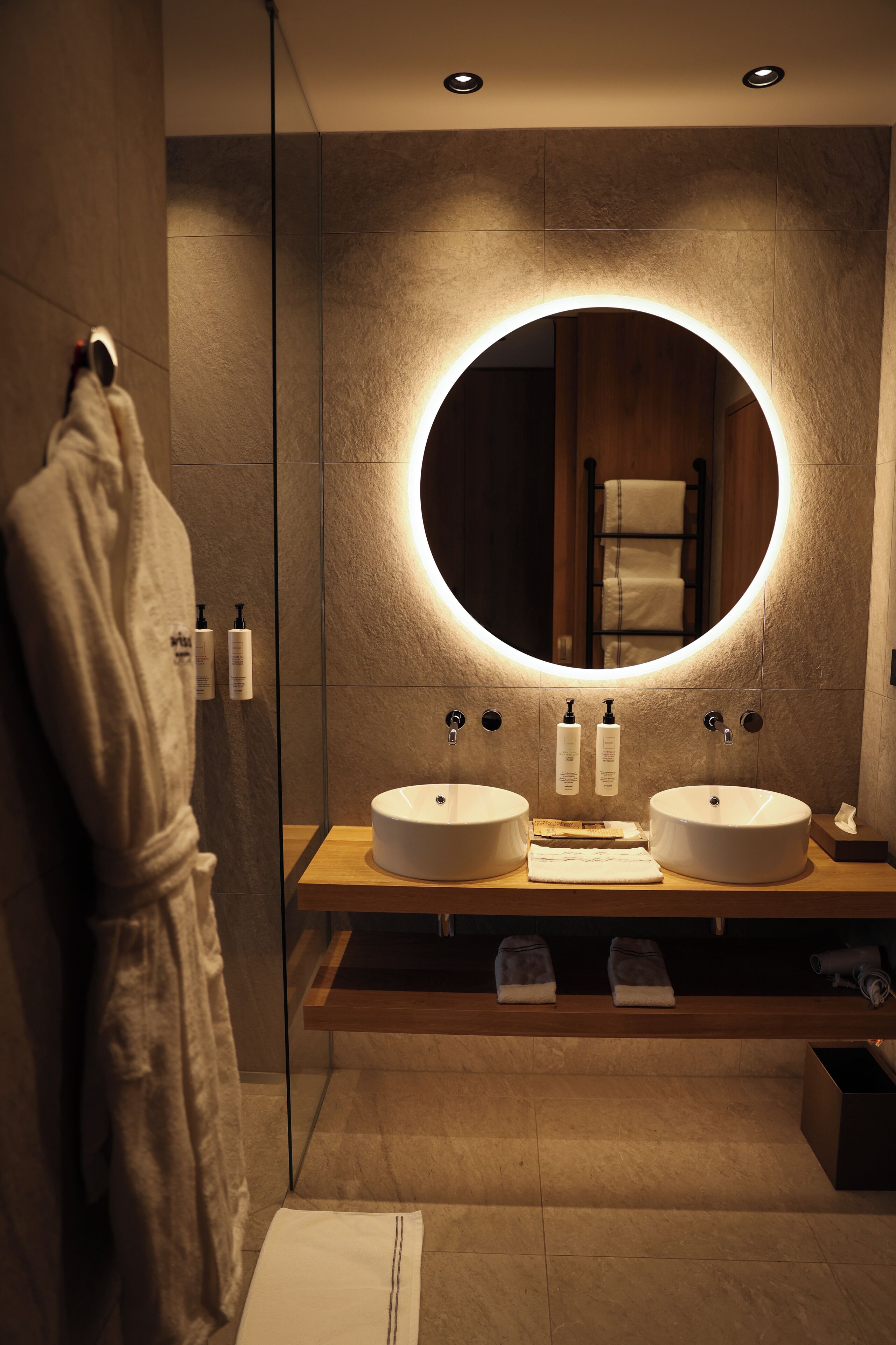 Een moderne badkamer met twee wastafels, een grote spiegel en een badjas aan de muur.
