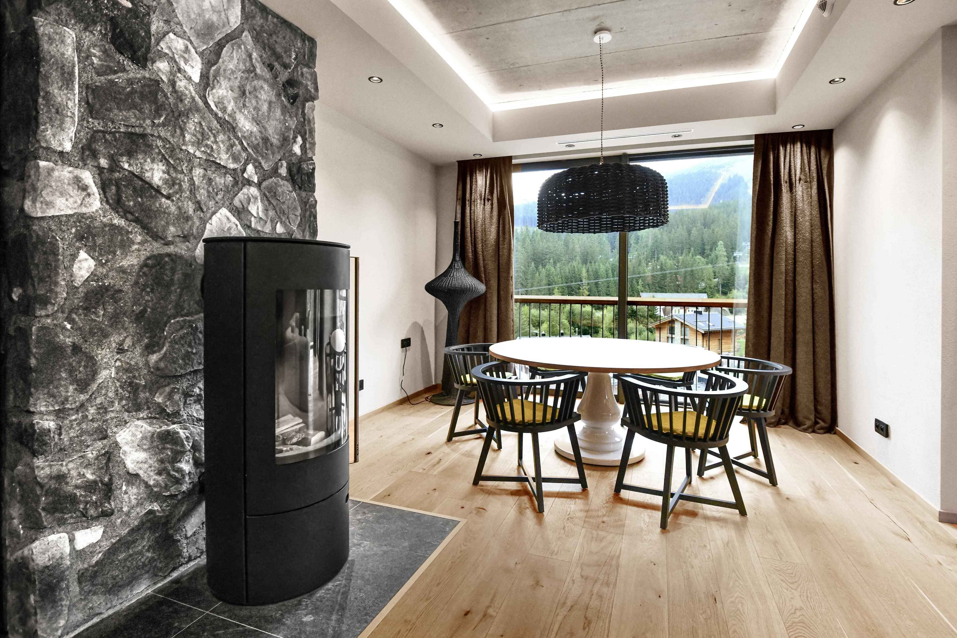 A modern dining area with a stone wall, a black fireplace, and a table with chairs.