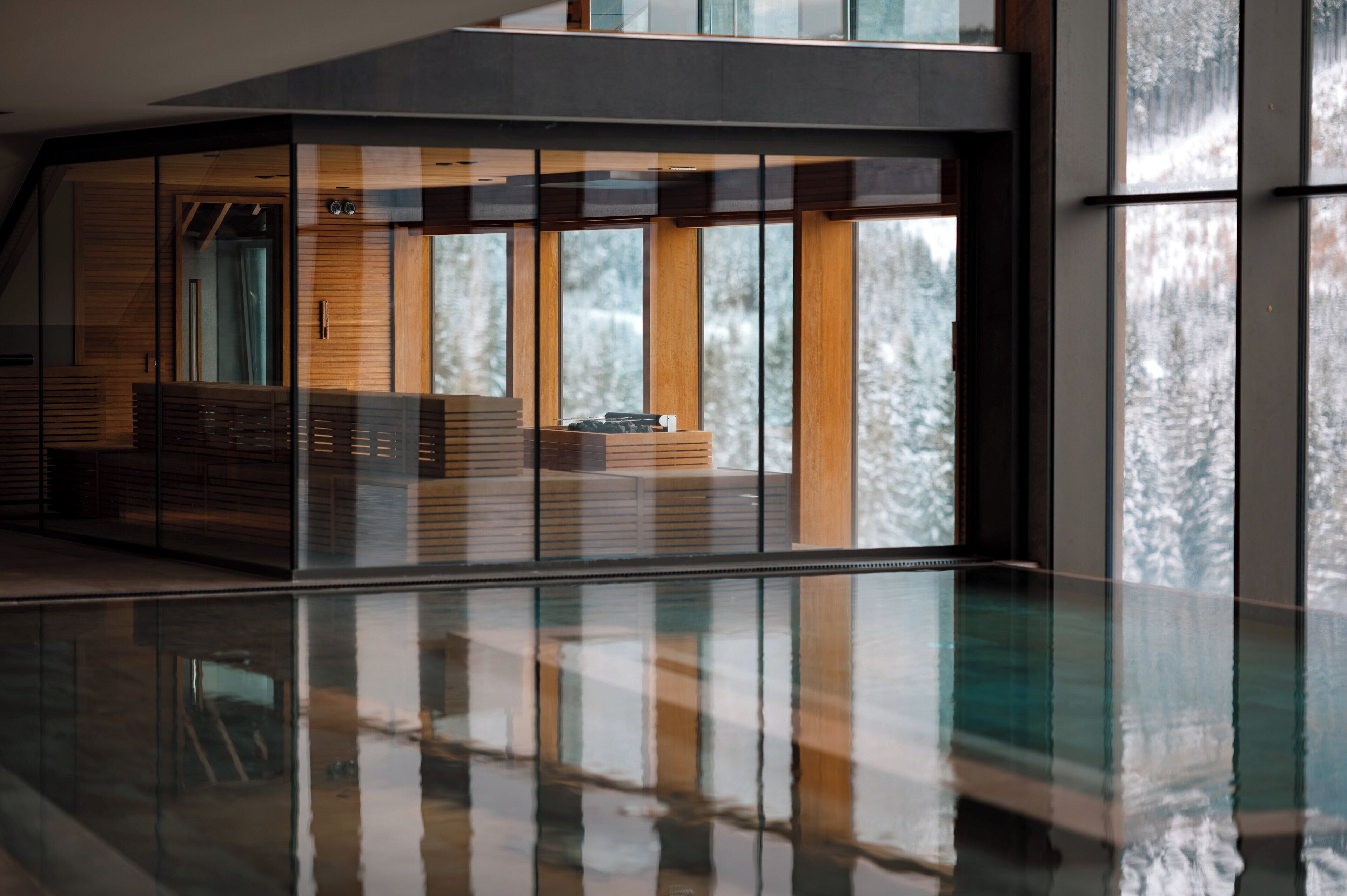 Un interior moderno con barandilla de cristal, paneles de madera y vistas a árboles nevados.