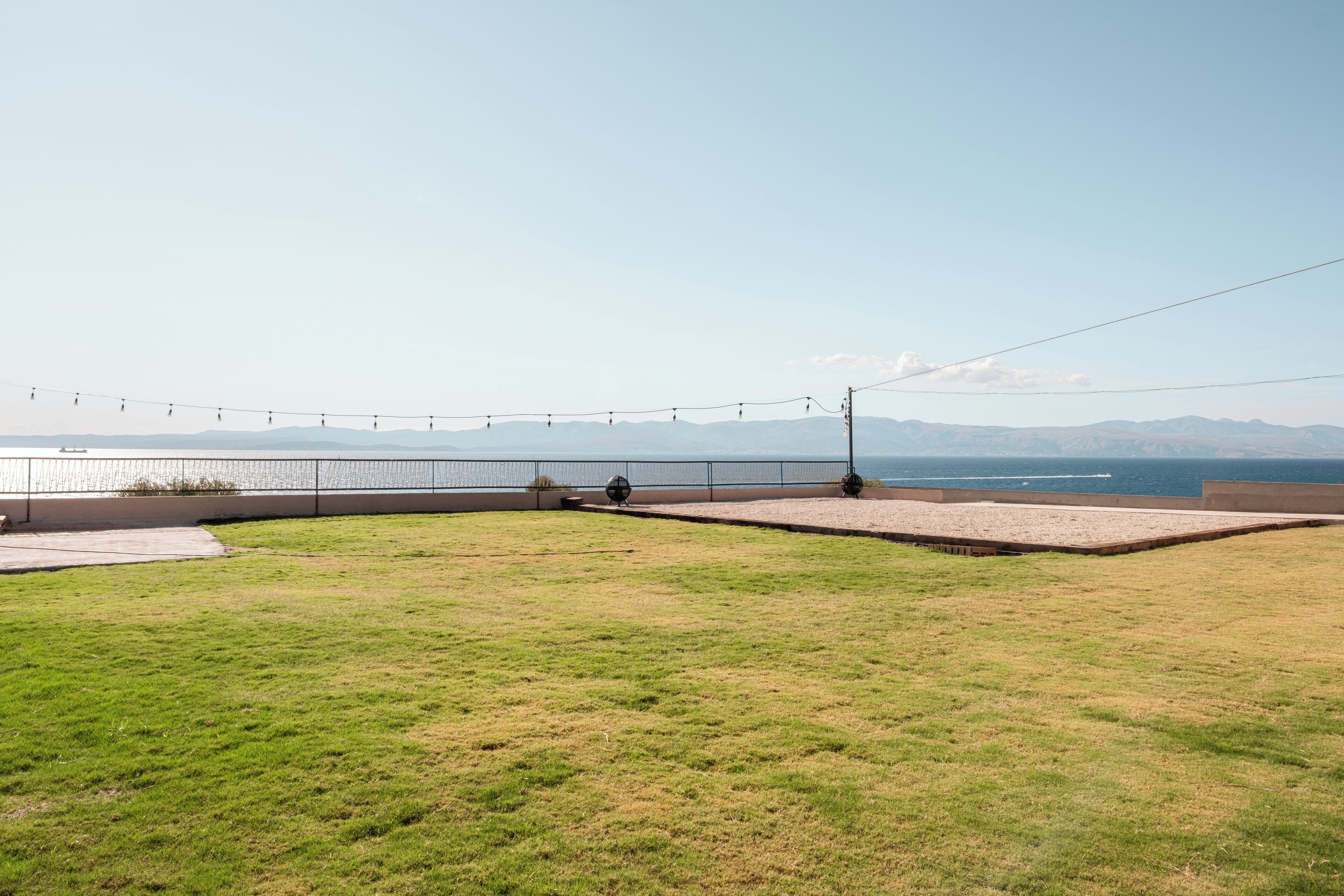 Zona verde con valla y luces cálidas, con vista a un cuerpo de agua y montañas distantes.