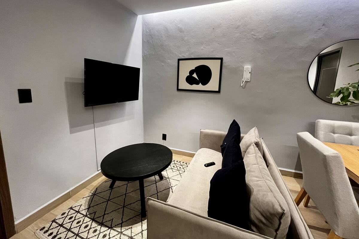 Ein modernes Wohnzimmer mit einer Couch, einem runden Tisch, einem Flachbildfernseher und einem gerahmten Kunstwerk an der Wand.