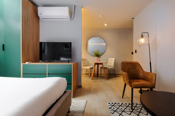 Una habitación de hotel moderna con cama, televisión, escritorio, silla, espejo redondo y lámpara de pie.