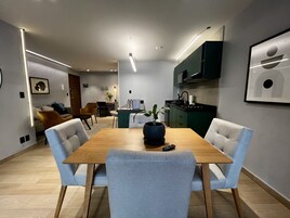 A modern kitchen with dark green cabinets, a wooden dining table, and light grey chairs.