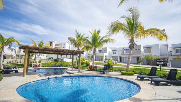 Una piscina con lettini, palme e moderni edifici sullo sfondo.