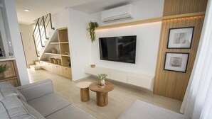Un soggiorno moderno con un divano, due tavolini rotondi in legno, una TV a schermo piatto montata a parete e una scala che conduce a un livello superiore.