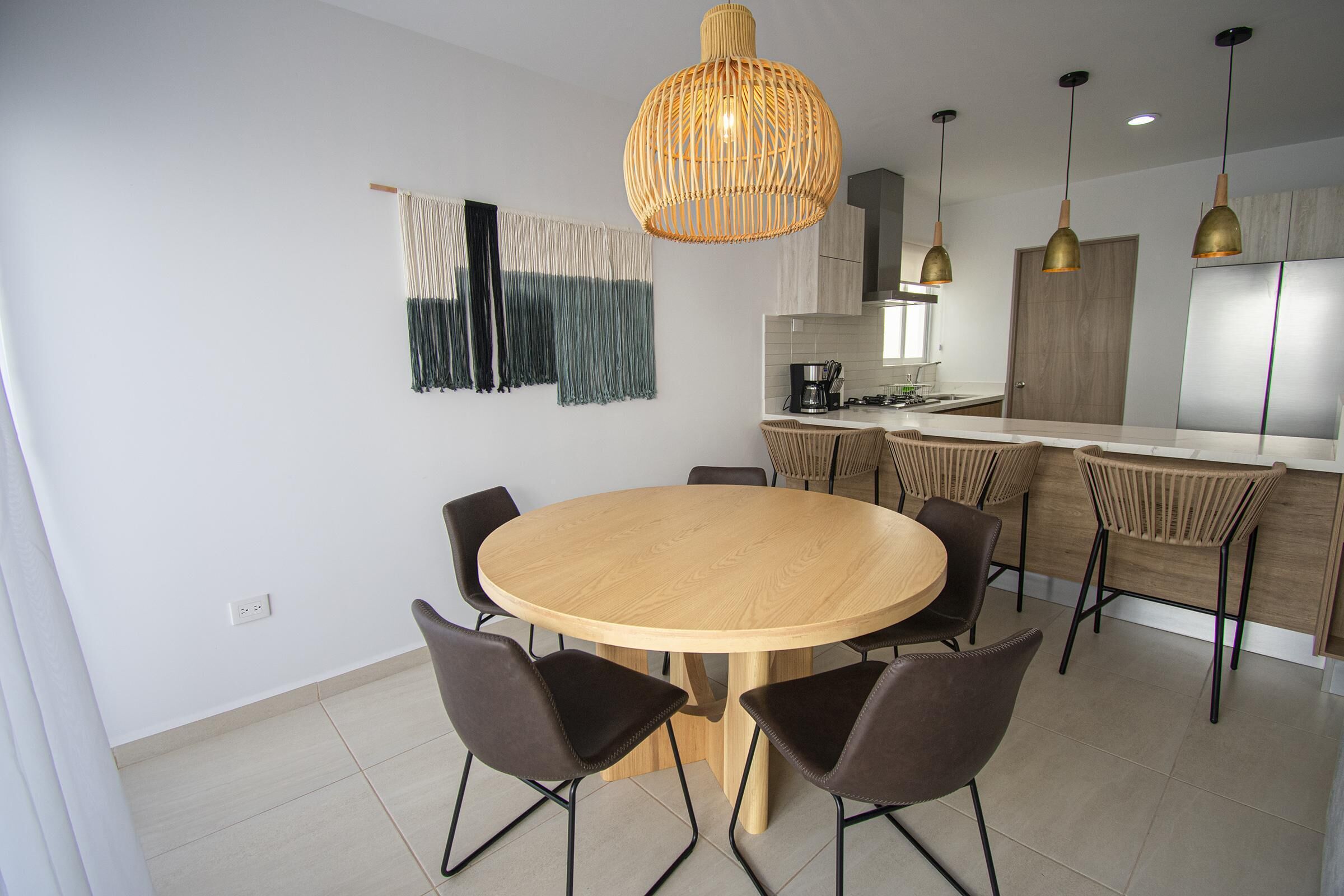 Eine moderne Küche mit einem runden Holztisch und Stühlen, einer Pendelleuchte sowie einer Kücheninsel mit Barhocker.