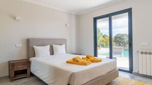 Quarto com cama, mesa de cabeceira, janela com vista para o exterior e porta para uma varanda.