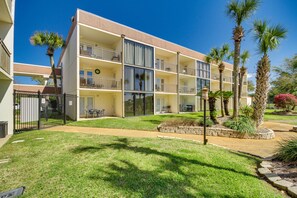 A multi-story hotel with balconies, a well-maintained lawn, and palm trees. - Biloxi Condo w/ Pool Access - Steps to Beach! (Biloxi)